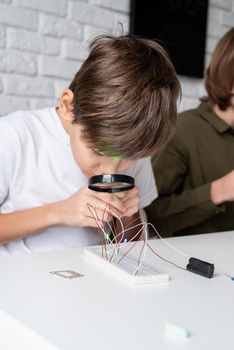 boy working with LED lights on experimental board for science project, using magnifying glass