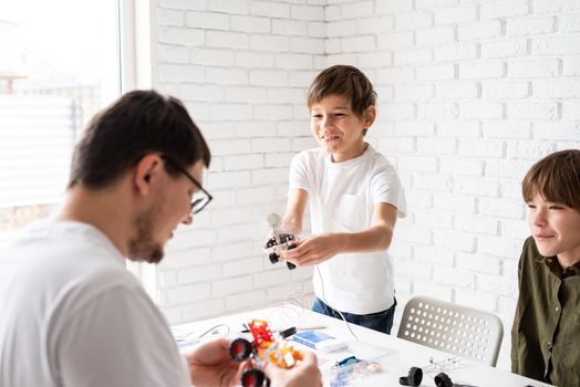 Father and his sons spending time together, having fun constructing robot cars at home