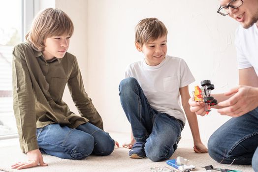 Young boys and teacher having fun constructing robot cars together at the workshop