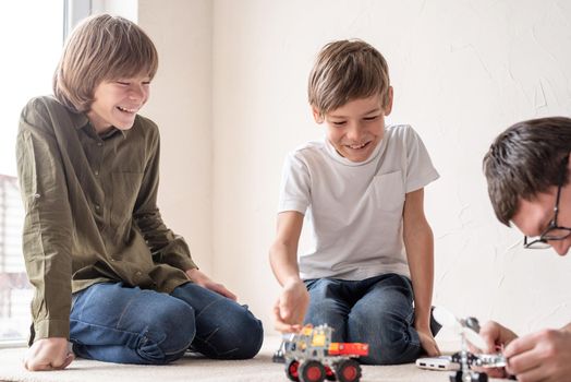 Father and his sons spending time together, having fun constructing robot cars at home sitting on the rug