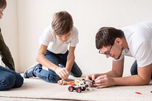 Father and his sons spending time together, having fun constructing robot cars at home sitting on the rug