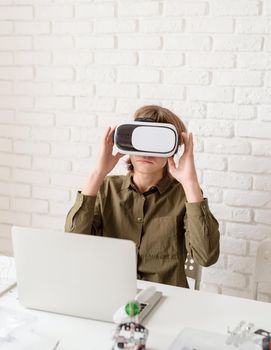 Nice teen boy in VR glasses sitting at the table playing game