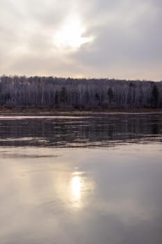 A beautiful, wide autumn river among the forests. A calm and quiet place with autumn colors. cloudy weather. The sun is reflected in the water.