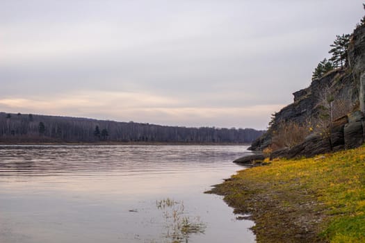 Beautiful, wide autumn river among forests and rocky shore. A calm and quiet place with autumn colors. Reflection of clouds in the water in good weather