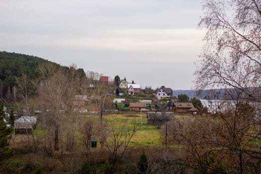 Houses along a beautiful, wide river in the middle of the forest. Calm and quiet place with autumn colors. In the middle of the river island. View from the top to the distance