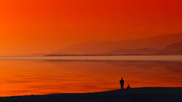 Seascape with orange sunset and silhouettes of people on the beach.