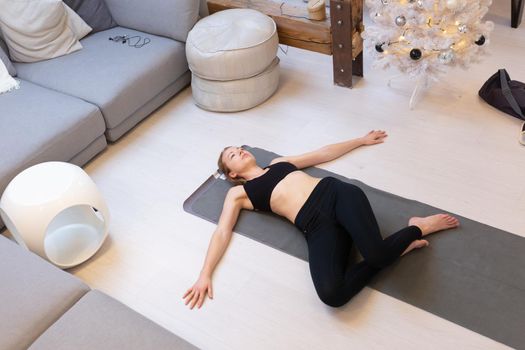 Beautiful blonde woman doing home workout indoors. Woman practice yoga at home. Fit girl using workout tutorials for healthy active lifestyle. Woman using quarantine for home workouts and stretching