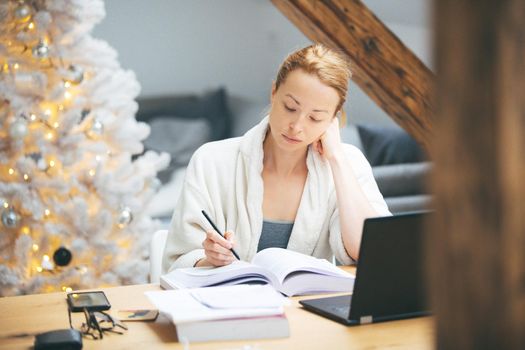 Young businesswoman wearing cosy warm bathrobe working remotly from home in winter Christmas time during 2020 corona virus pandemic. Work from home, selter in place, concept.