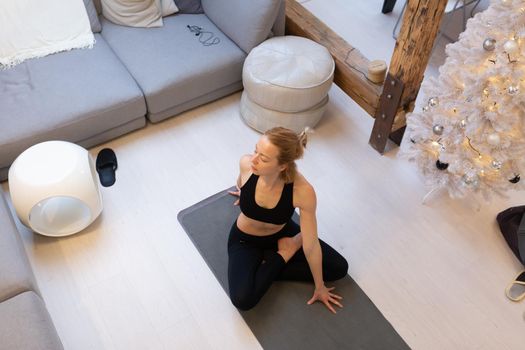 Beautiful blonde woman doing home workout indoors. Woman practice yoga at home. Fit girl using workout tutorials for healthy active lifestyle. Woman using quarantine for home workouts and stretching