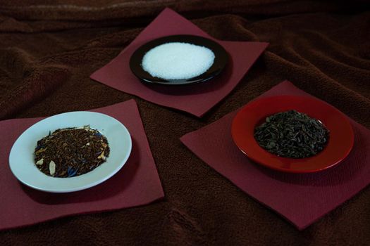 Three dishes with sugar, tea, and shading on red napkins and brown tablecloth