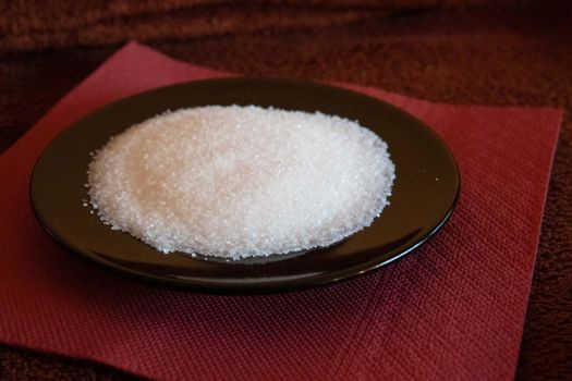 Black plate with sugar on brown tablecloth