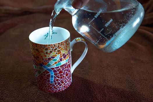 Pitcher of boiling water pouring the water over a cup of colored