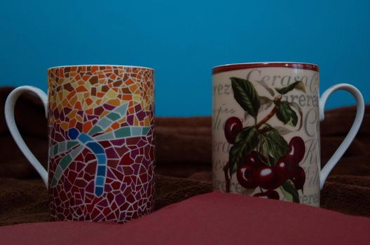 Two tea cups with beautiful prints on brown tablecloth and blue background