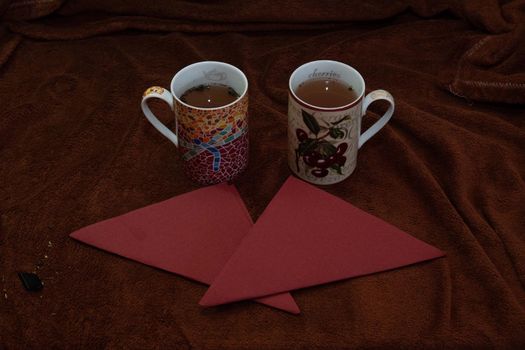 Two cups of tea with a couple of red napkins over a brown butter