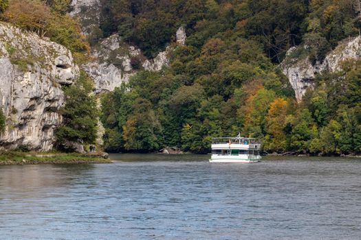 Passenger ship passing Danube breakthrough near Kelheim, Bavaria, Germany in autumn with gravel bank in foreground and limestone formations in the background