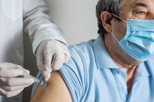 Doctor holding syringe with Covid-19 or coronavirus vaccine. Medical worker vaccinating an elderly patient against flu, influenza, pneumonia or coronavirus.