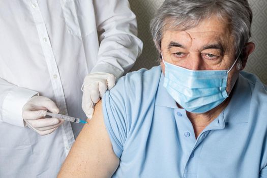 Senior elderly man being vaccinated against coronavirus by a male doctor. General practitioner vaccinating an elderly patient against flu, influenza, pneumonia or coronavirus.