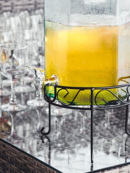 Glass barrel of cold lemonade. Transparent container with tap for soft drinks. Catering services for parties and celebrations. Outdoor bar.