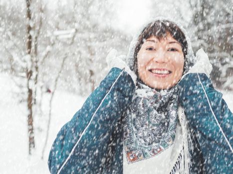 Smiling woman is playing with knitted hat. Fun in snowy winter forest. Woman laughs as she walks through wood. Sincere emotions.