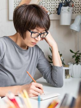 Woman with short hair cut is drawing in notebook. Calming hobby, antistress leisure. Artist at work. Cozy workplace.