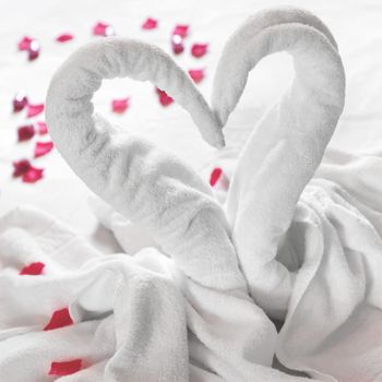 Towel swans on the bed, sprinkled with red petals. Ideal for events and concepts. Honeymoon, engagement, Valentine's Day. Love.
