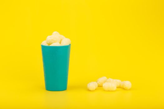 Still life with corn curls in blue plastic cup with against yellow background with copy space. Concept of unhealthy junk food with fat
