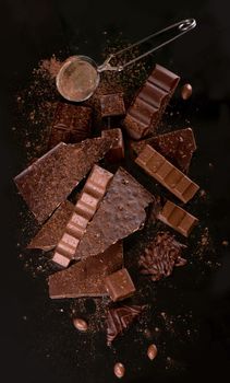 Broken chocolate pieces and cocoa powder on wooden background