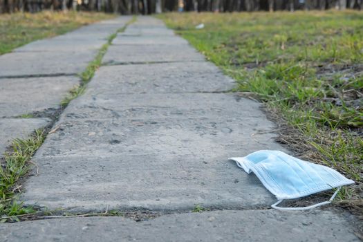 a used, carelessly discarded medical anti virus mask lies on the footpath on the way to the city park