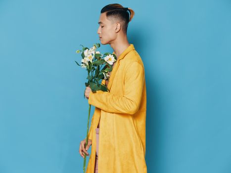 Cheerful Asian man in a yellow coat with a bouquet of flowers. High quality photo