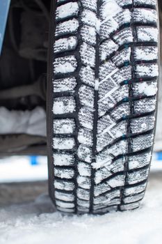 Car tires on the winter road are covered with snow. A car on a snow-covered alley. A car wheel in the snow.