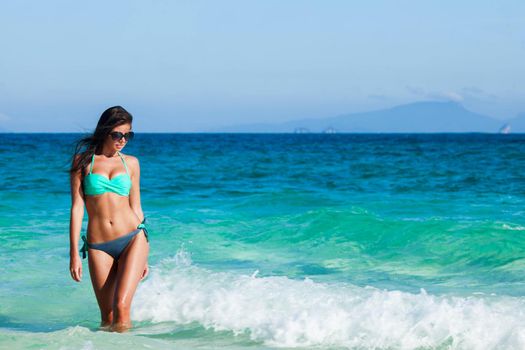 Pretty smiling girl in bikini standing in transparent water of tropical sea