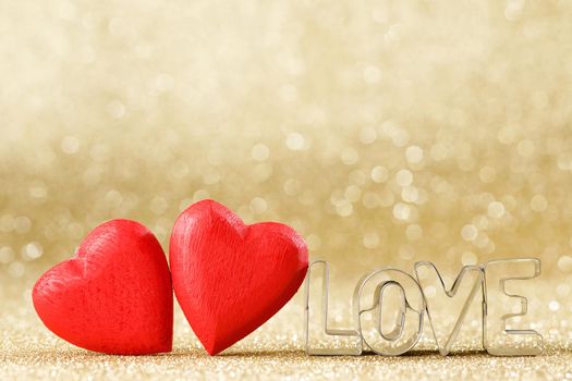 Two red handmade wooden hearts and word love on golden bright glitter lights bokeh background
