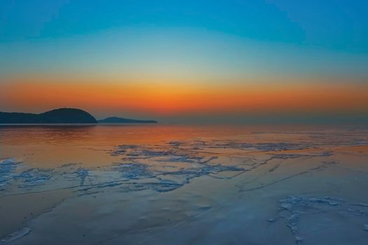 Seascape with bright orange sunset and ice floes at the coastline. Vladivostok, Primorsky Krai