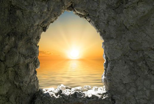 A stone wall with a window opening from which you can see the sea and the sunset