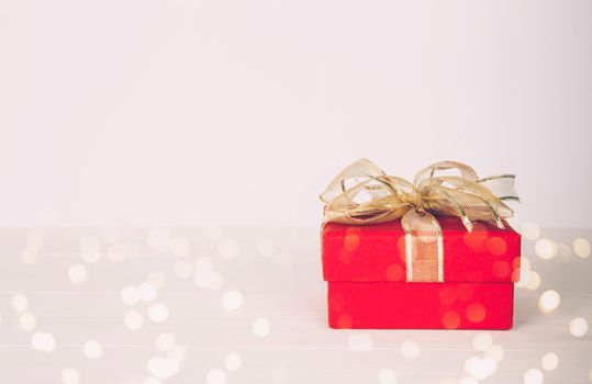 Red gift box on wooden table with bokeh background, love and romance, presents in celebration and anniversary with surprise on desk, happy birthday, copy space, nobody, valentine day concept.