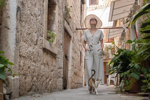 Beautiful blonde young female traveler wearing straw sun hat sightseeing and enjoying summer vacation in an old traditional costal town at Adriatic cost, Croatia.