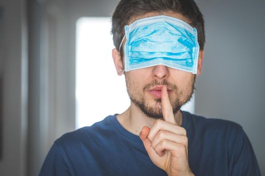 Young angry man with face mask over the eyes is doing a psst! gesture