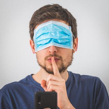 Young angry man with face mask over the eyes is doing a psst! gesture