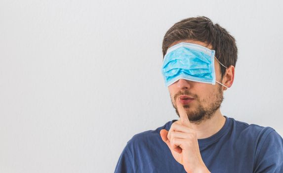 Young angry man with face mask over the eyes is doing a psst! gesture