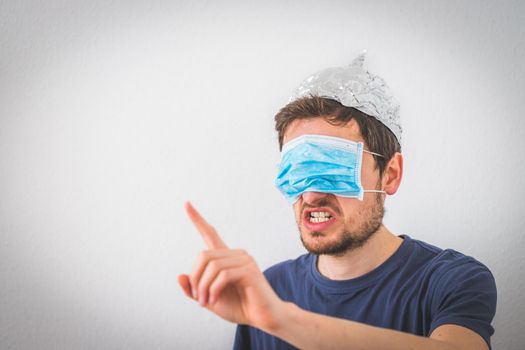 Young angry man with aluminum cap and face mask over the eyes is gesturing angry. Conspiracy theory concept.