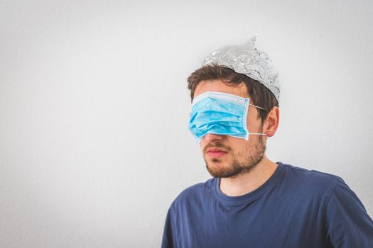 Young angry man with aluminum cap and face mask. Conspiracy theory concept.