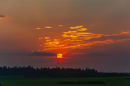 Sunset. The sun sets behind clouds against a background of green forest and fields. Stock photography