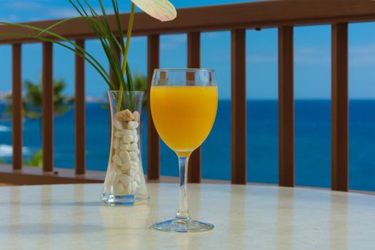 glass of orange juice and a bowl of green grass stand on the table against the blue sea. Stock photo