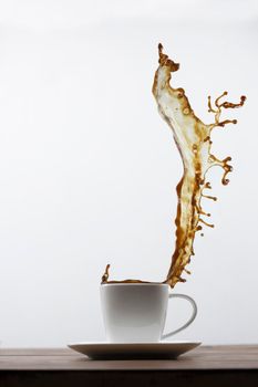 Splashing of coffee in white cup and falling coffee beans on white background.