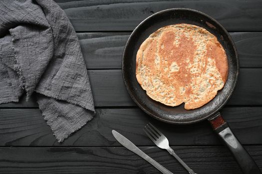 Hot pancake in black pan on black table with flour.