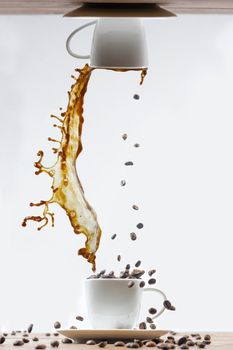 Splashing of coffee in white cup and falling coffee beans on white background.