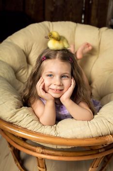A beautiful little girl has a cute fluffy Easter duckling on her head.