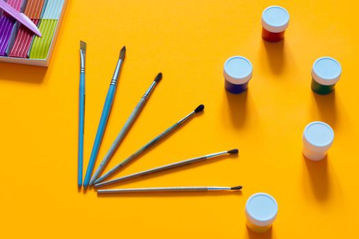 Brushes, gouache and plasticine are laid out on an orange table