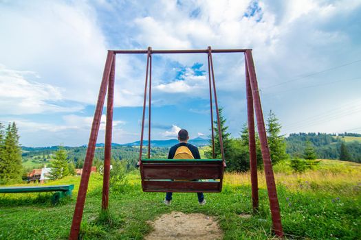 The guy tourist sit on the swing and enjoy amzing nature landscape of summer Karpaty mountains.