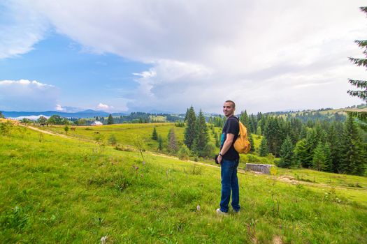 A guy travels with a yellow backpack through picturesque places with beautiful mountain landscapes.